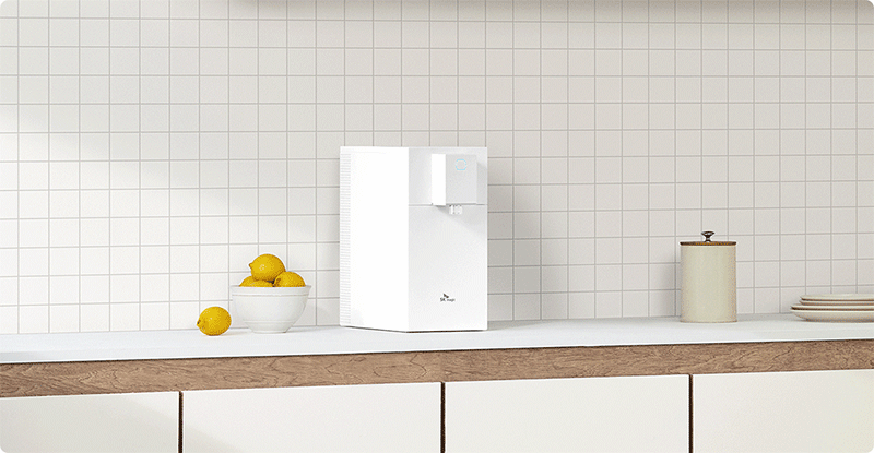 정수기 온도 활용 가이드: 가장 탁월하게 맛있는 정수기 온수 온도는? 화이트 타일 배경의 깔끔한 주방에 놓인 SK매직 핑크색 정수기와 레몬 연출 이미지