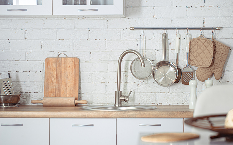 소형 아파트 및 1~2인 가구 필수 가전 추천: 좁은 주방 공간 활용을 위한 슬림한 가정용 정수기 구독 가이드. 화이트 브릭 벽면과 원목 상판으로 꾸며진 모던한 주방 인테리어 연출 이미지